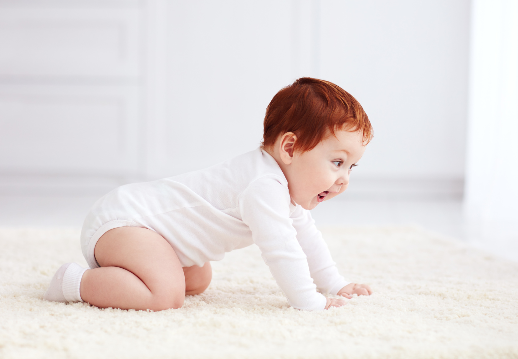 happy, nine months old baby crawling on carpet at home Janod